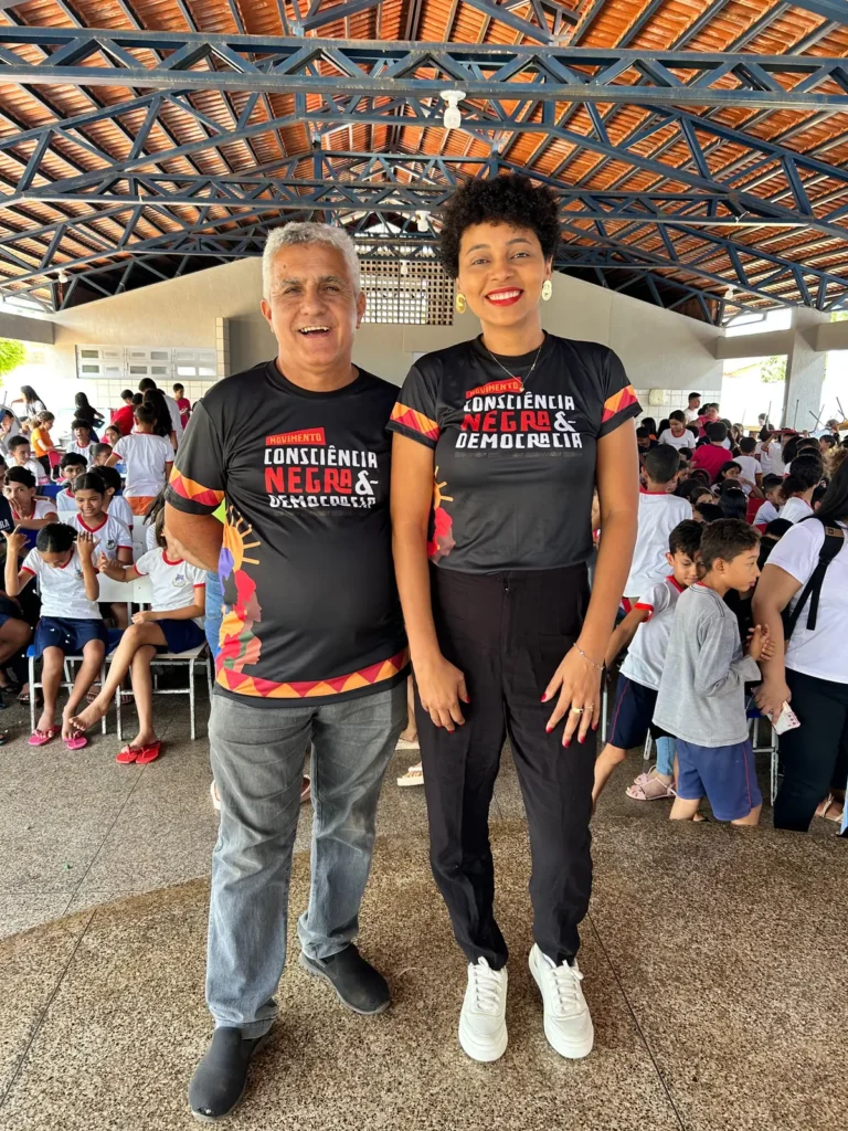 Dois integrantes do movimento posam diante de crianças reunidas em atividade escolar