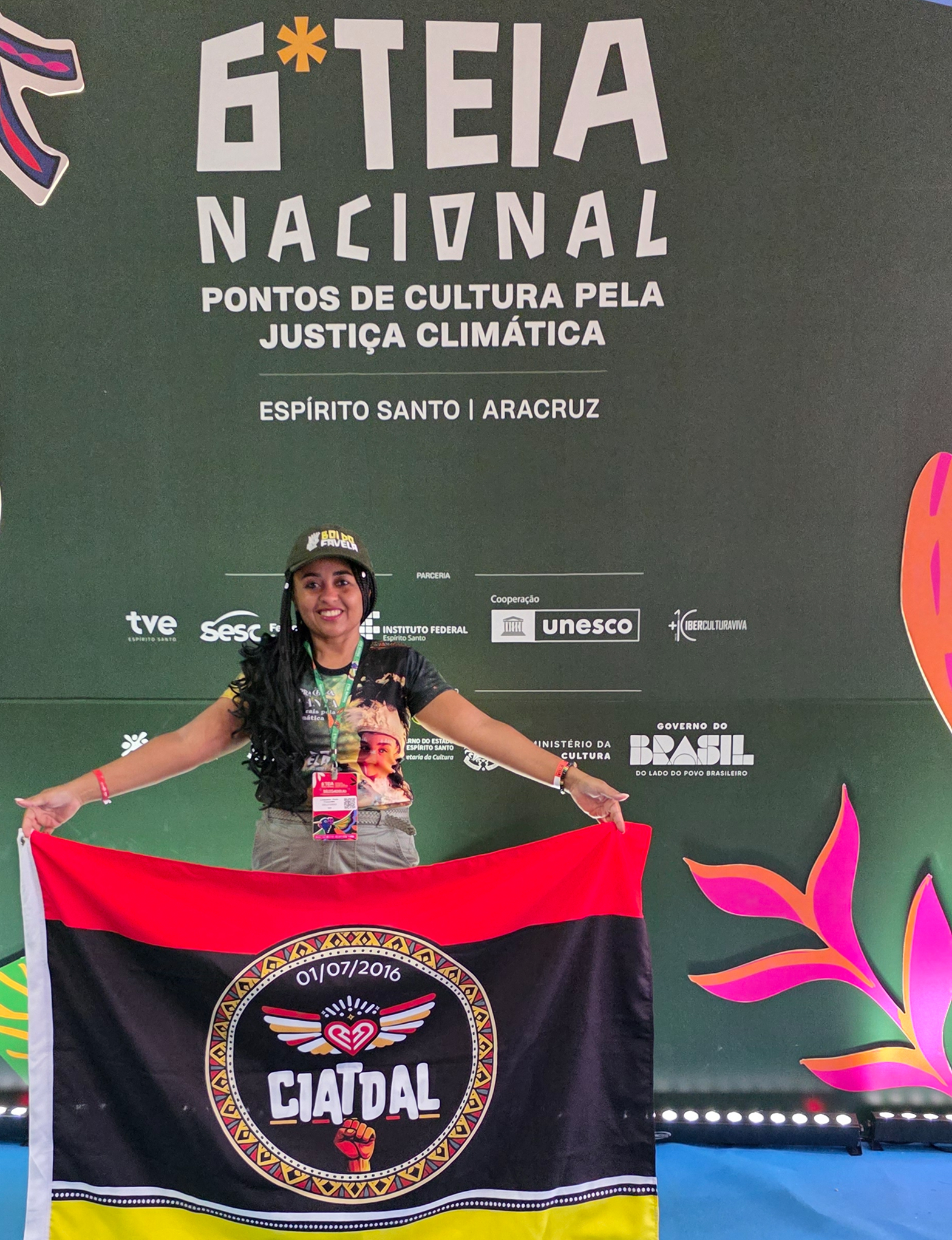 Presidente da CIATDAL segurando a bandeira da organização no painel oficial da 6ª TEIA Nacional em Aracruz