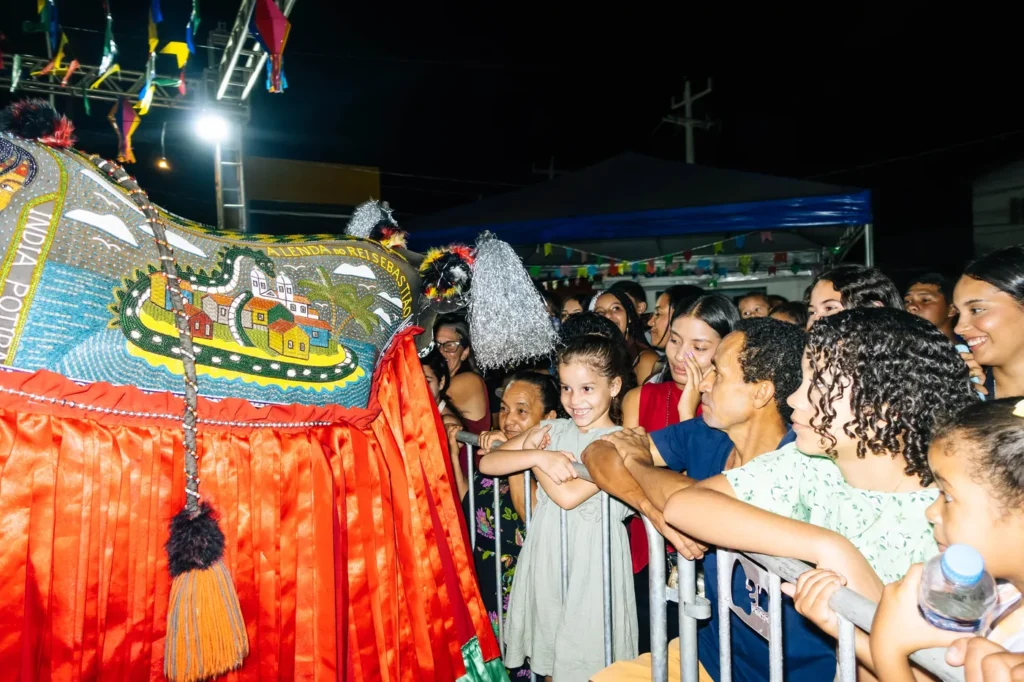 O boi do Boi do Favela chega perto da grade e crianças e adultos acompanham a apresentação bem de perto