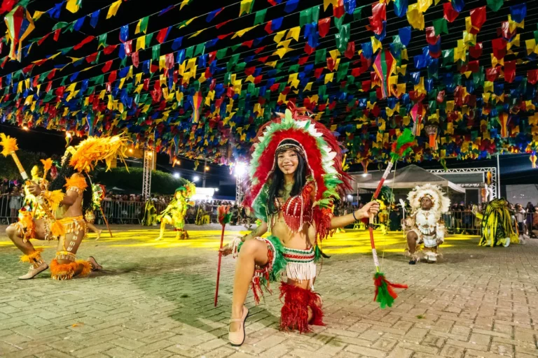 Brincante do Boi do Favela com cocar vermelho dança sob as bandeirinhas do arraial