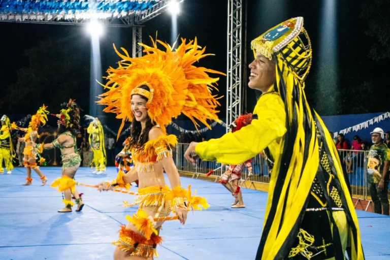 Dois brincantes do Boi do Favela com figurino amarelo dançam juntos na arena