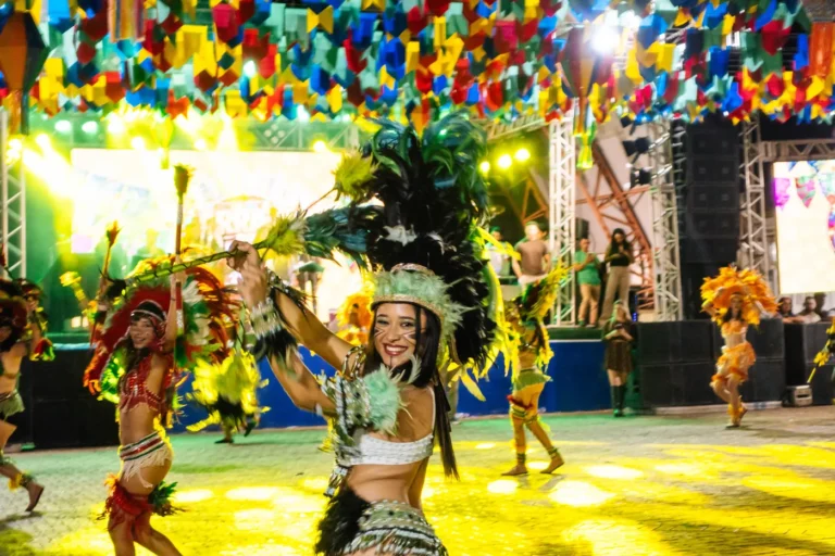 Dançarina do Boi do Favela sorri com cocar verde durante apresentação em arraial