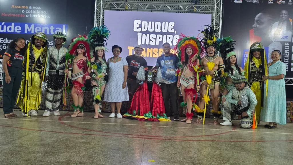 Grupos culturais com figurinos posam no palco sob o lema Eduque, Inspire, Transforme
