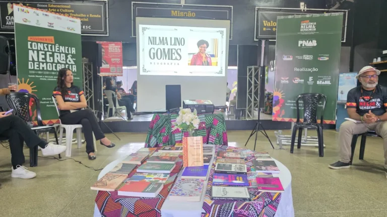 Mesa com livros de autores negros e a projeção com a biografia de Nilma Lino Gomes ao fundo