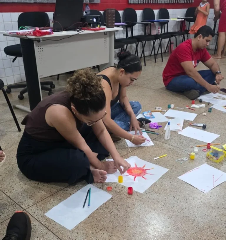 Educadoras e crianças pintam desenhos no chão durante oficina de arte