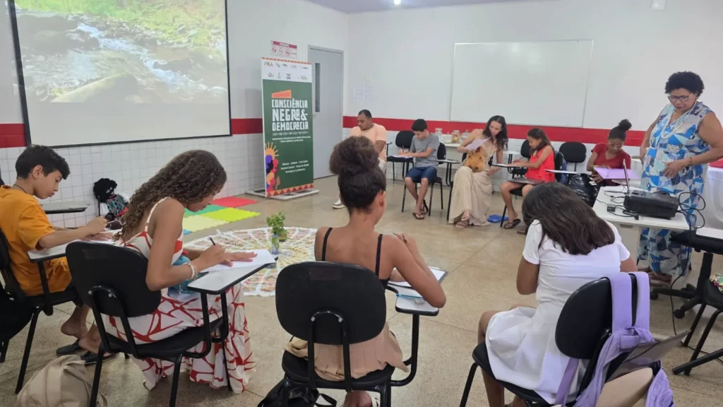 Estudantes em roda participam de atividade do movimento em sala de aula, com o banner ao fundo