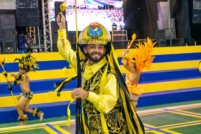Brincante do Boi do Favela com figurino amarelo e chapéu bordado ergue o braço em comemoração