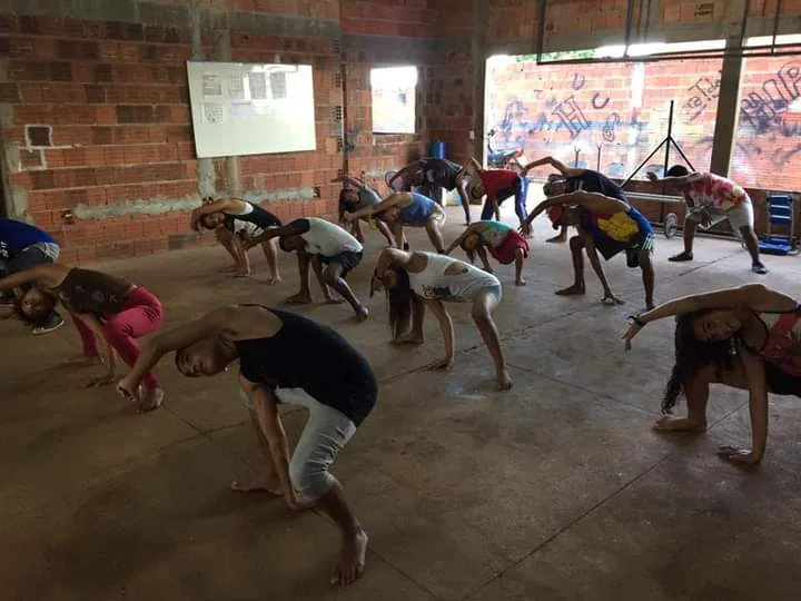 Turma de jovens faz alongamento durante aula de dança da CIATDAL, em galpão de tijolo aparente