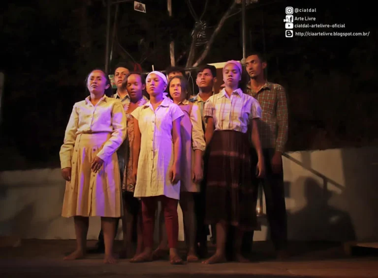 Elenco da CIATDAL em cena de espetáculo teatral à noite, com figurinos de época