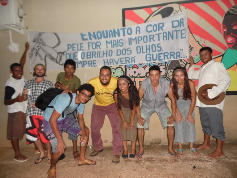 Integrantes da CIATDAL posam diante de faixa pintada à mão sobre racismo, em atividade cultural