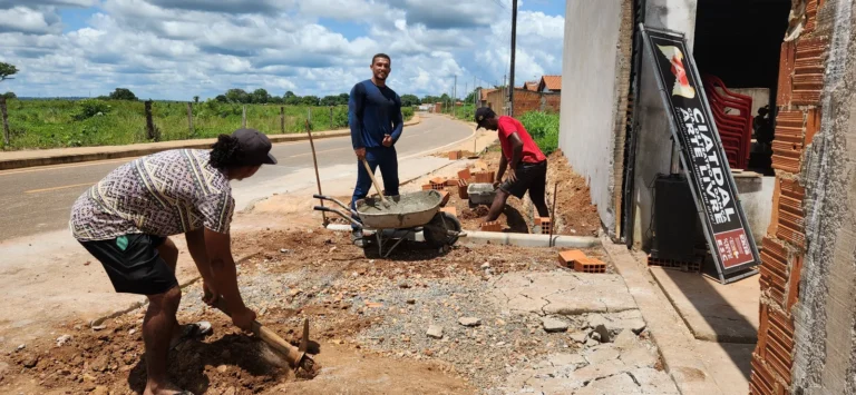 Três pessoas trabalham na obra da calçada da sede da CIATDAL, com carrinho de mão e tijolos