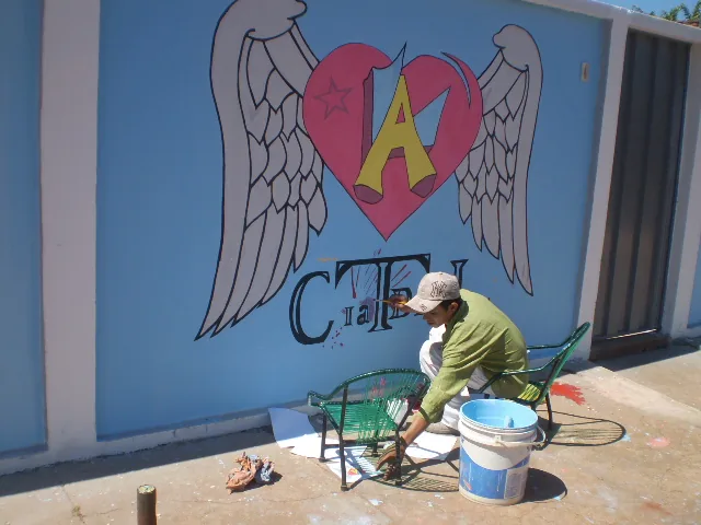 Pintor termina o mural do coração com asas, símbolo da CIATDAL, na parede azul da sede